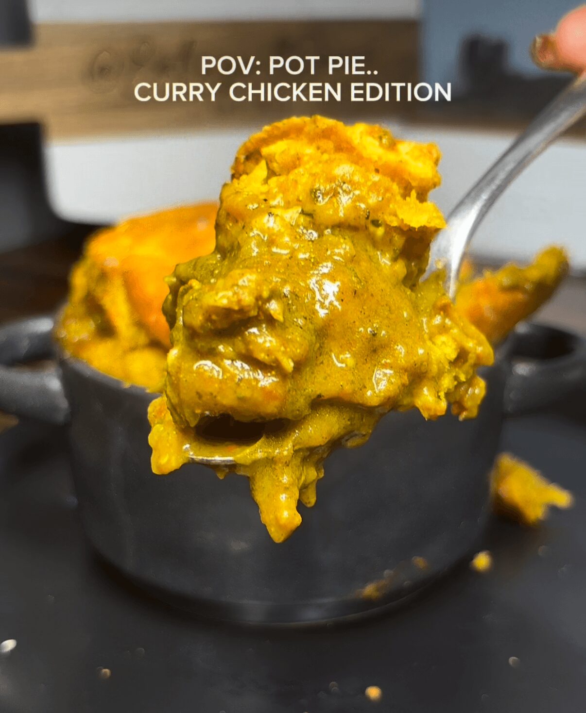 Close-up of a spoonful of curry chicken pot pie filling with a golden crust in the background.
