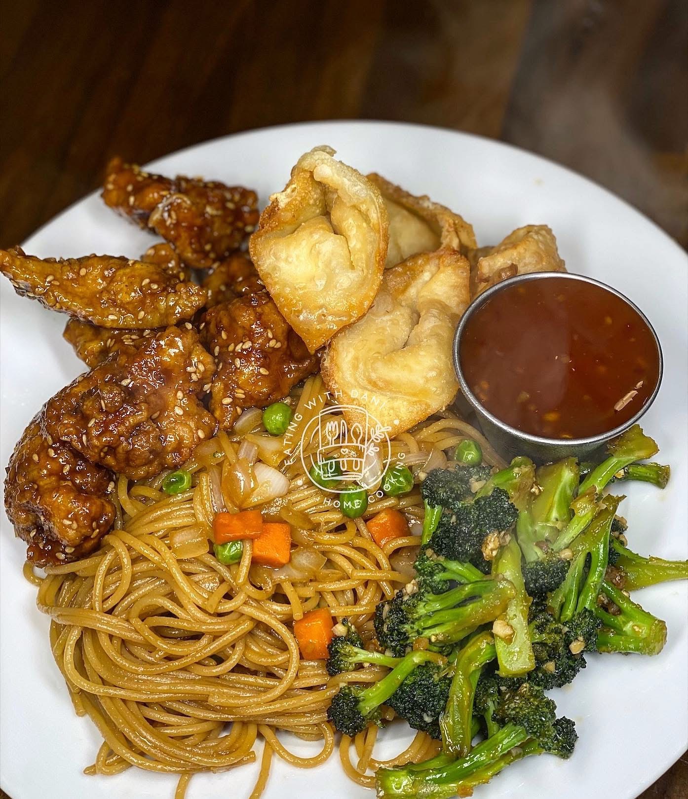 Plate with fried chicken, fried fish, broccoli, noodles, and a small cup of sauce, on a white dish.