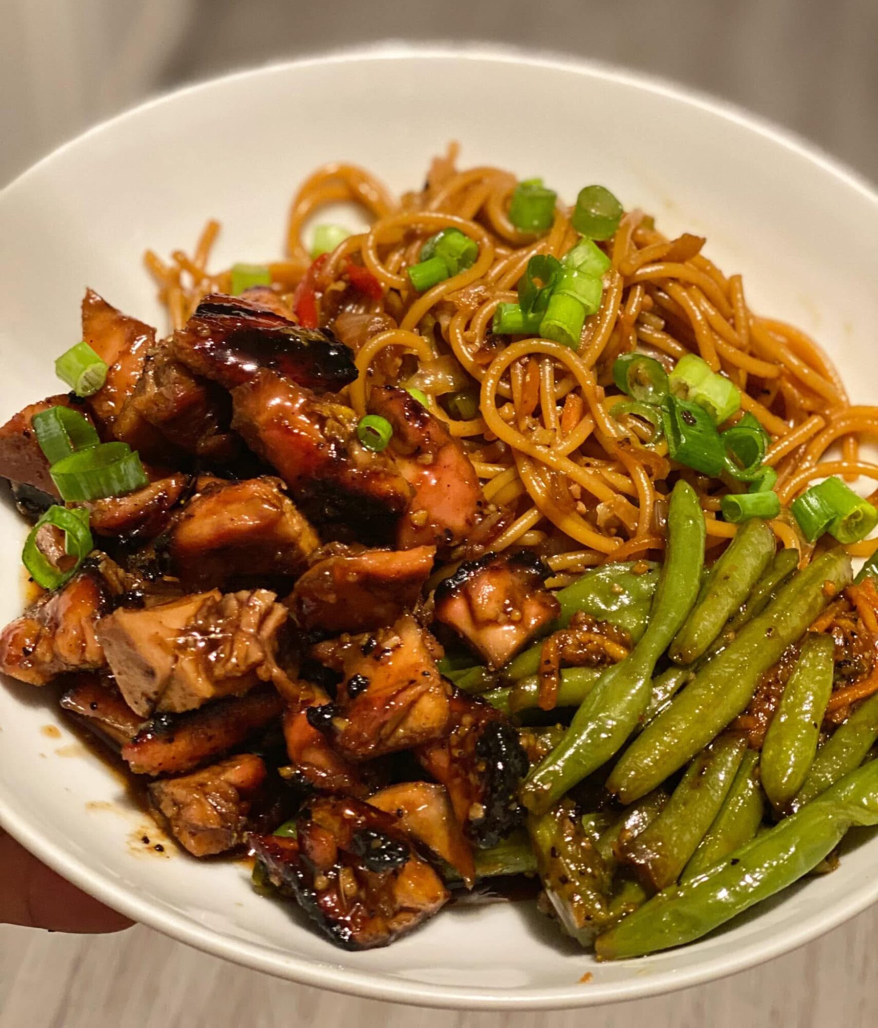 Bowl with noodles, grilled chicken, and green beans, garnished with chopped green onions.