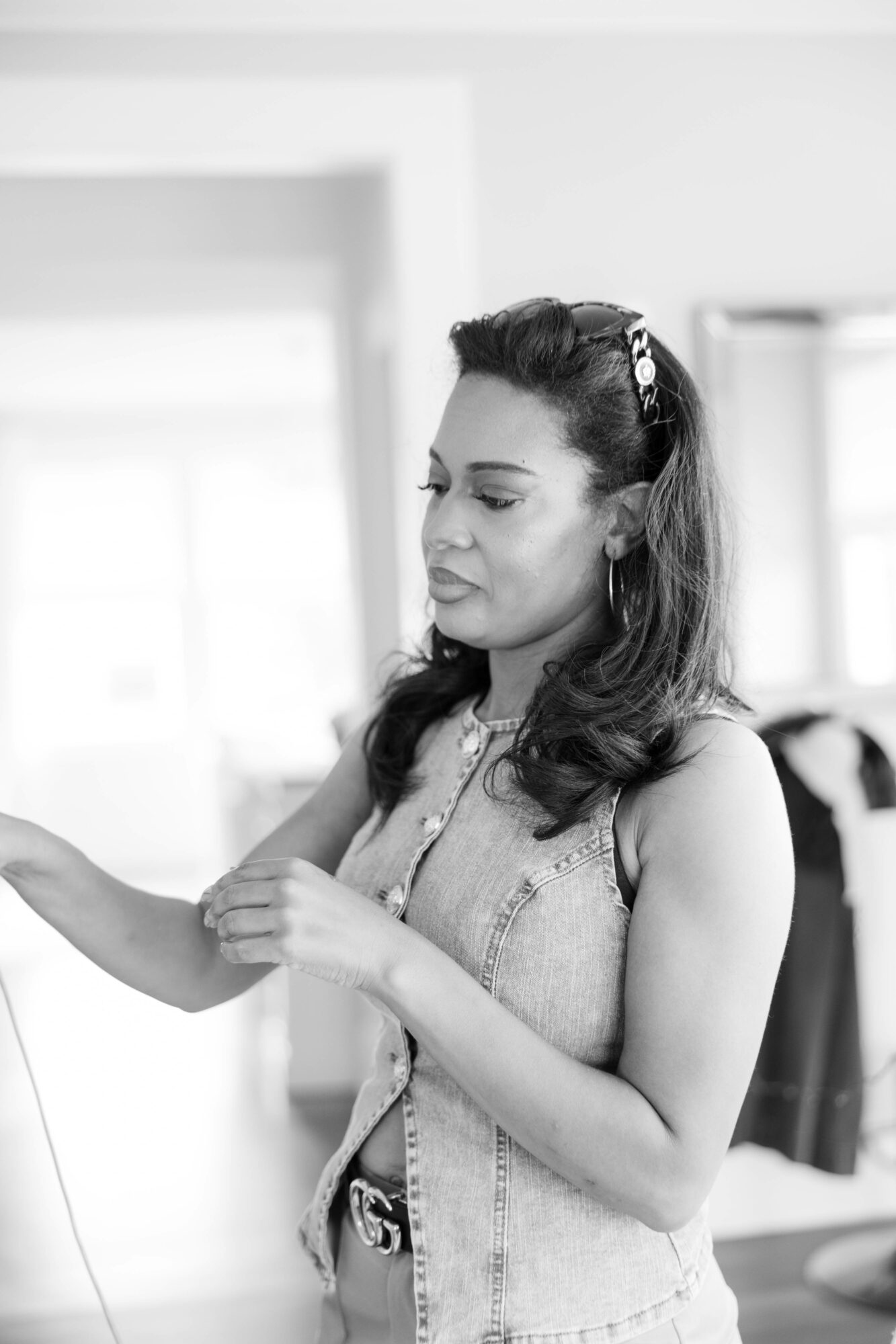 Woman with dark hair and a headband, wearing a sleeveless top, looking to the side in a bright room.