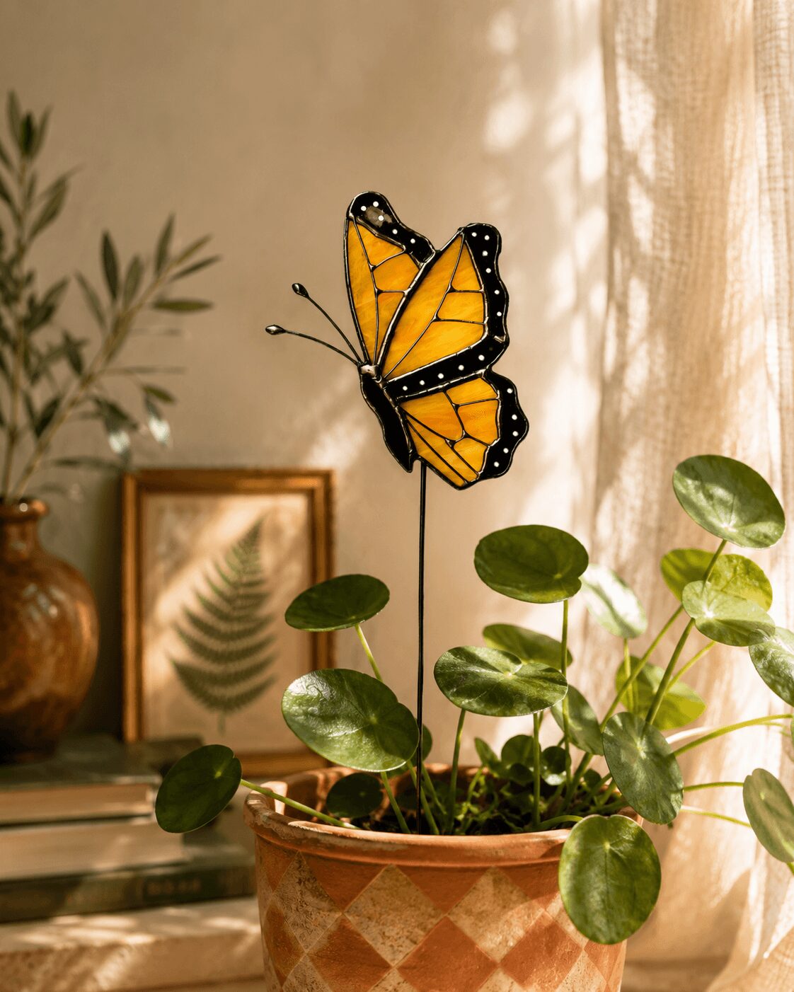 A butterfly with orange and black wings perched on a green plant in a pot, near a window with sunlight.