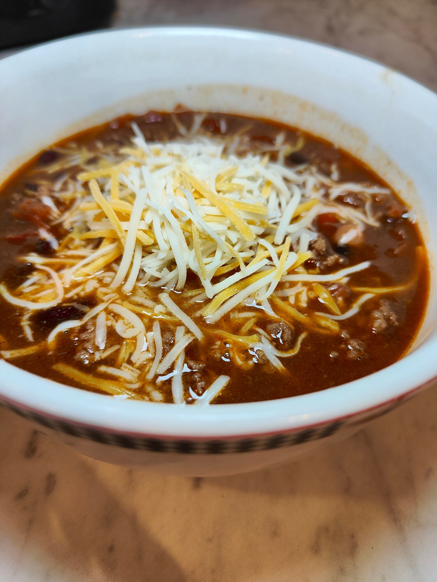 Bowl of spicy noodle soup topped with shredded cheese, with a dark broth and noodles visible.