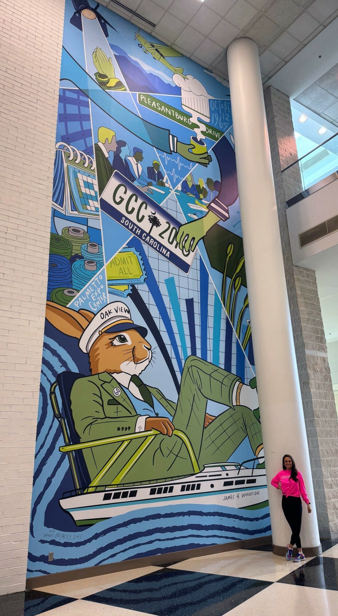 Large colorful mural with a person in a boat, buildings, and various abstract elements, located indoors near a white pillar.