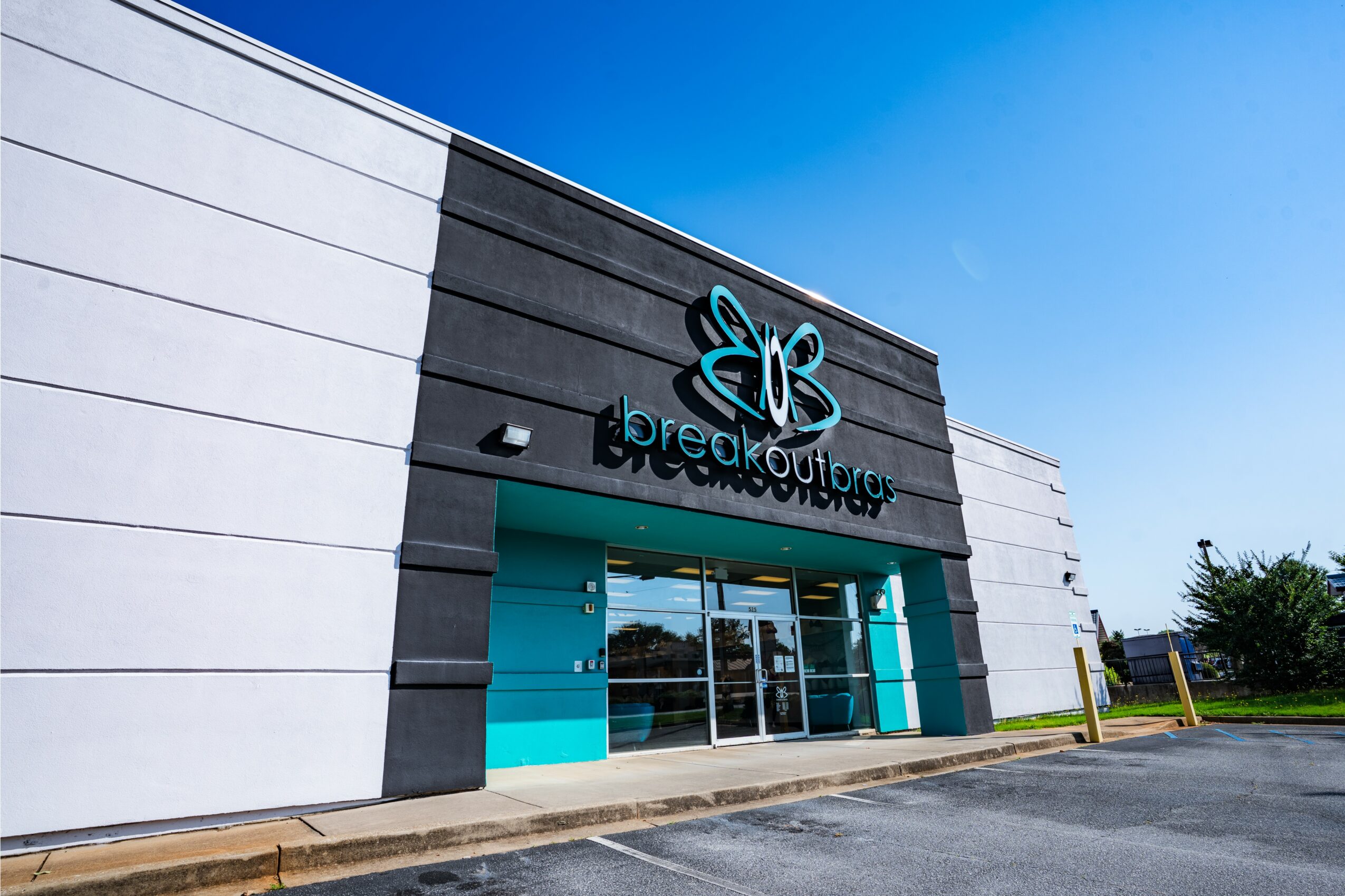 Storefront with a butterfly logo and sign reading 'breakout' on a sunny day, with a parking lot in front.