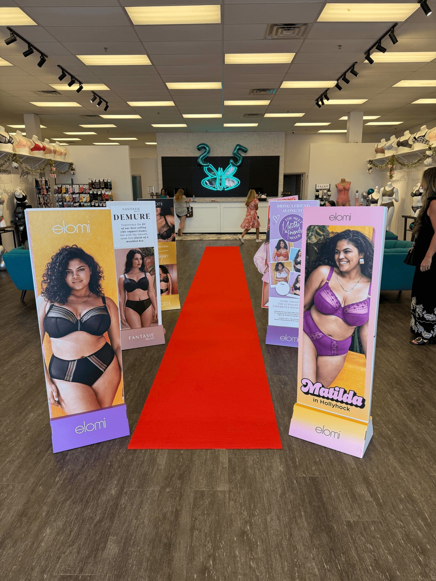 Indoor store with promotional posters of women in lingerie, red carpet aisle, and store displays in background.