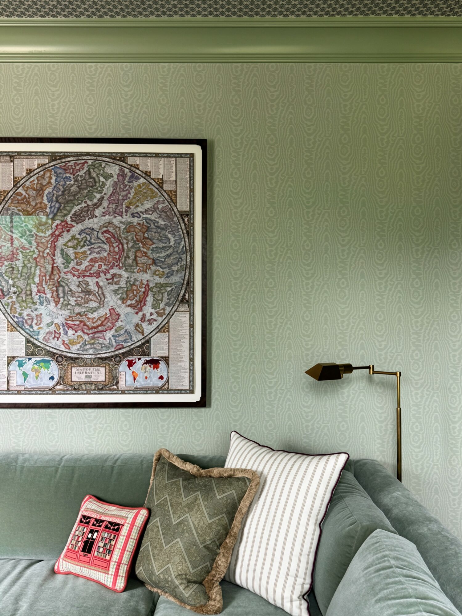 Living room with green wall, framed artwork, sofa with pillows, and a wall-mounted lamp.