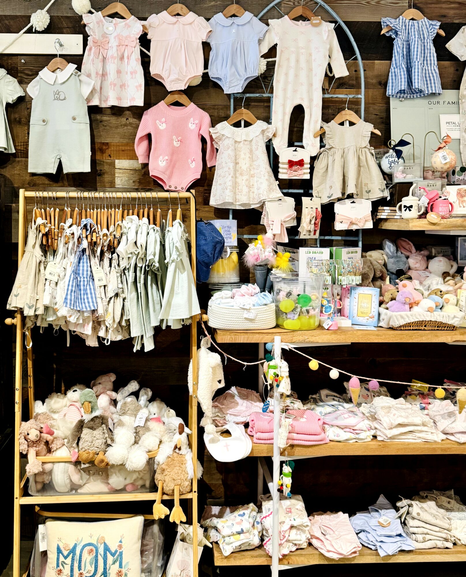 Display of baby clothes, toys, and accessories on shelves and racks in a store, with stuffed animals and gift items visible.