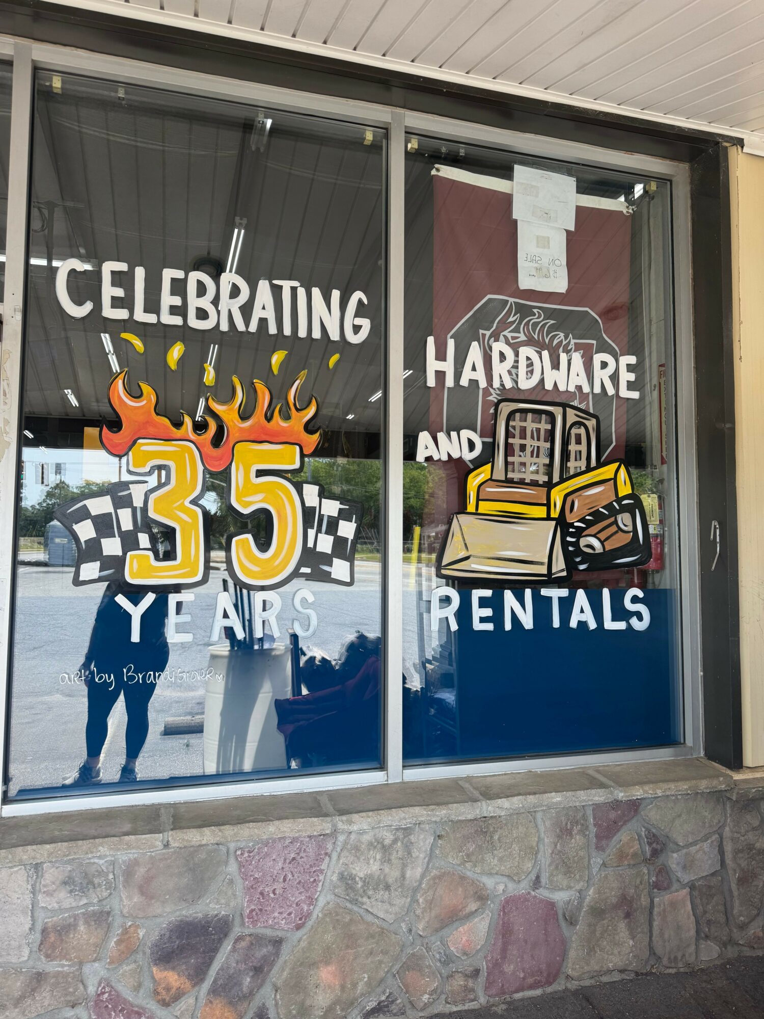 Glass door with celebration sign, cartoon toolbox, and text indicating 35 years of hardware and rentals.