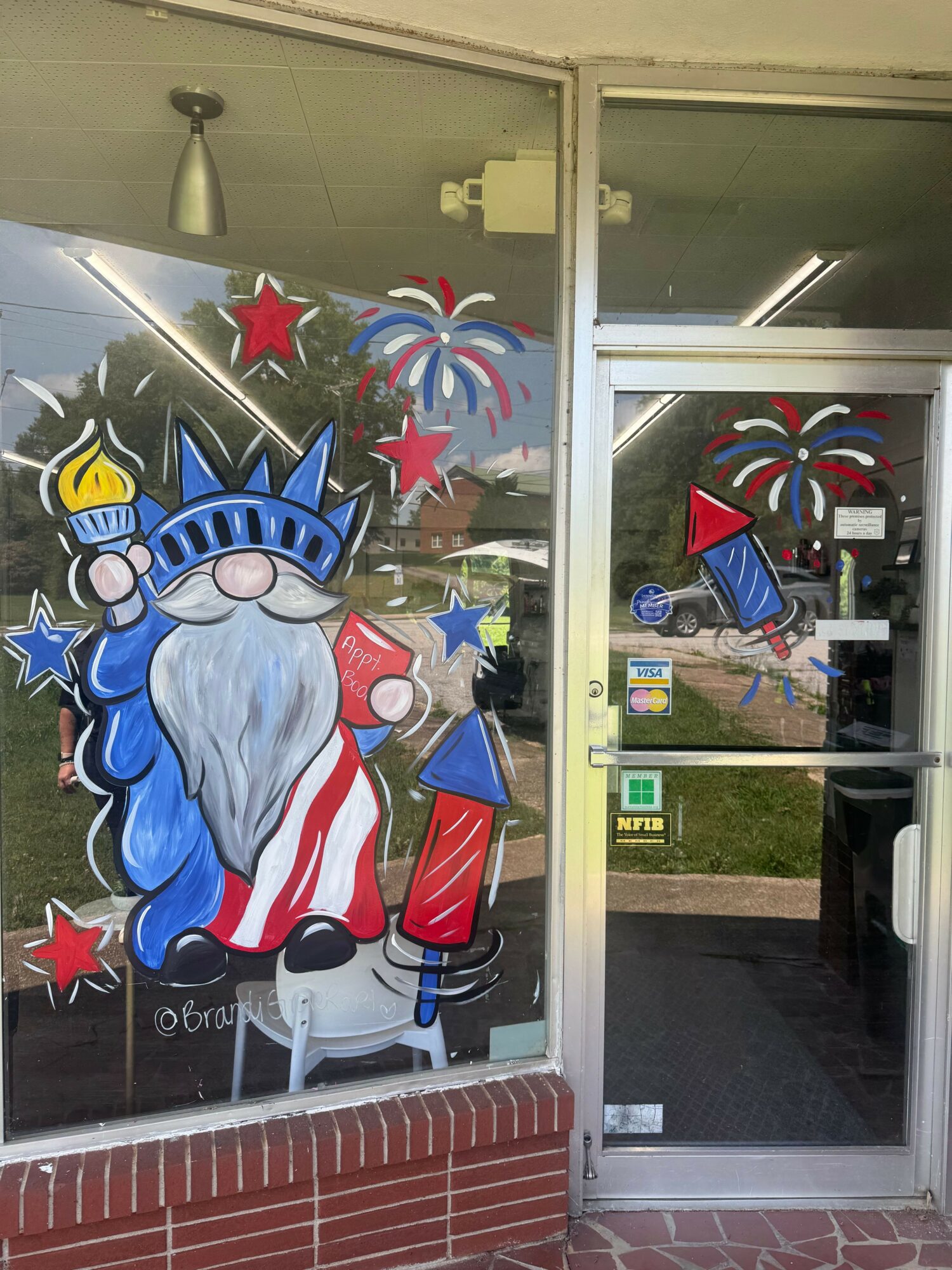 Decorative window with patriotic-themed stickers, including a large figure of Uncle Sam, stars, and fireworks, with a brick wall outside.