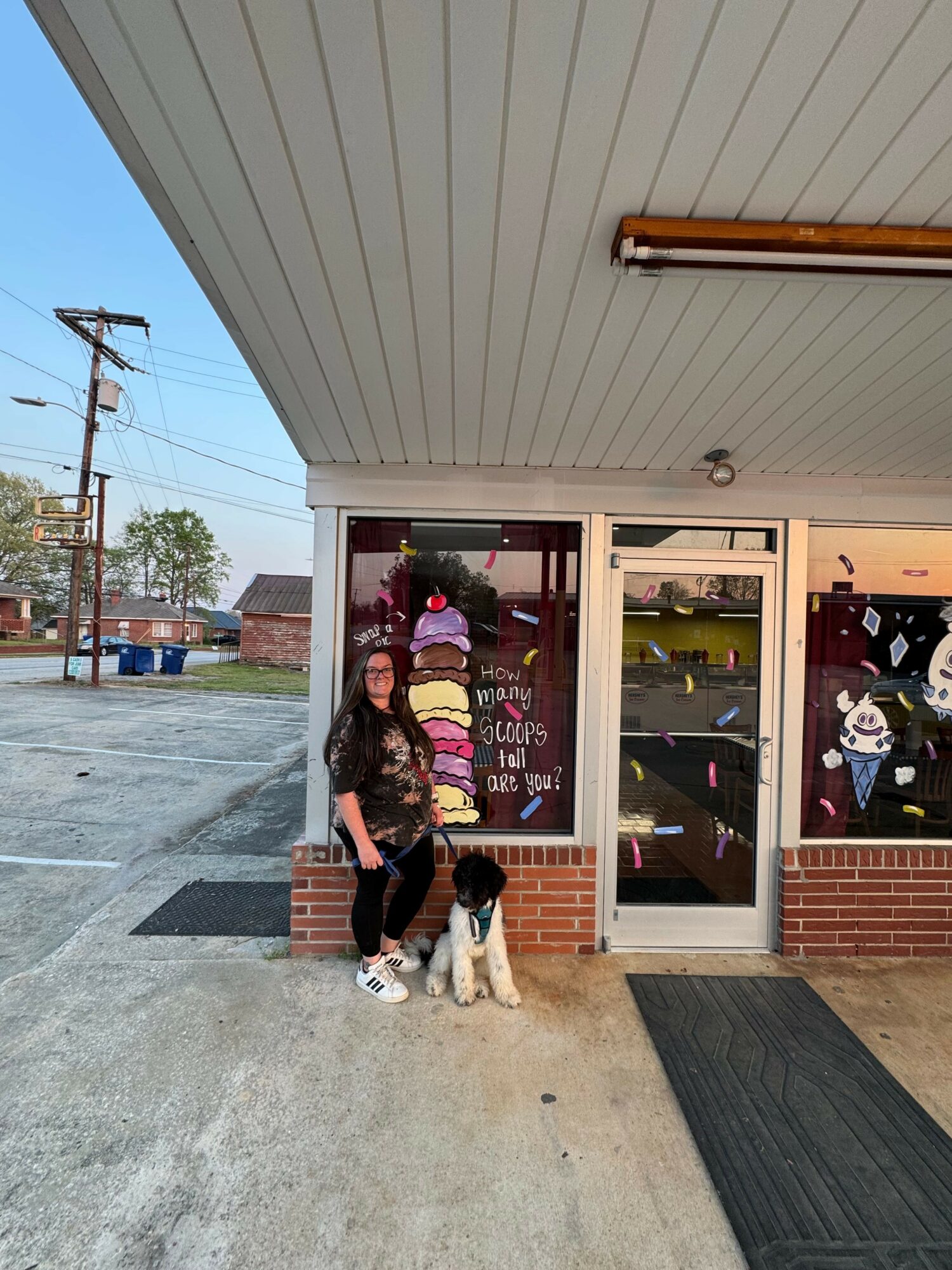 Two children sit outside a store with glass doors, one child with a white jacket and the other with a colorful sweater, on a concrete sidewalk.