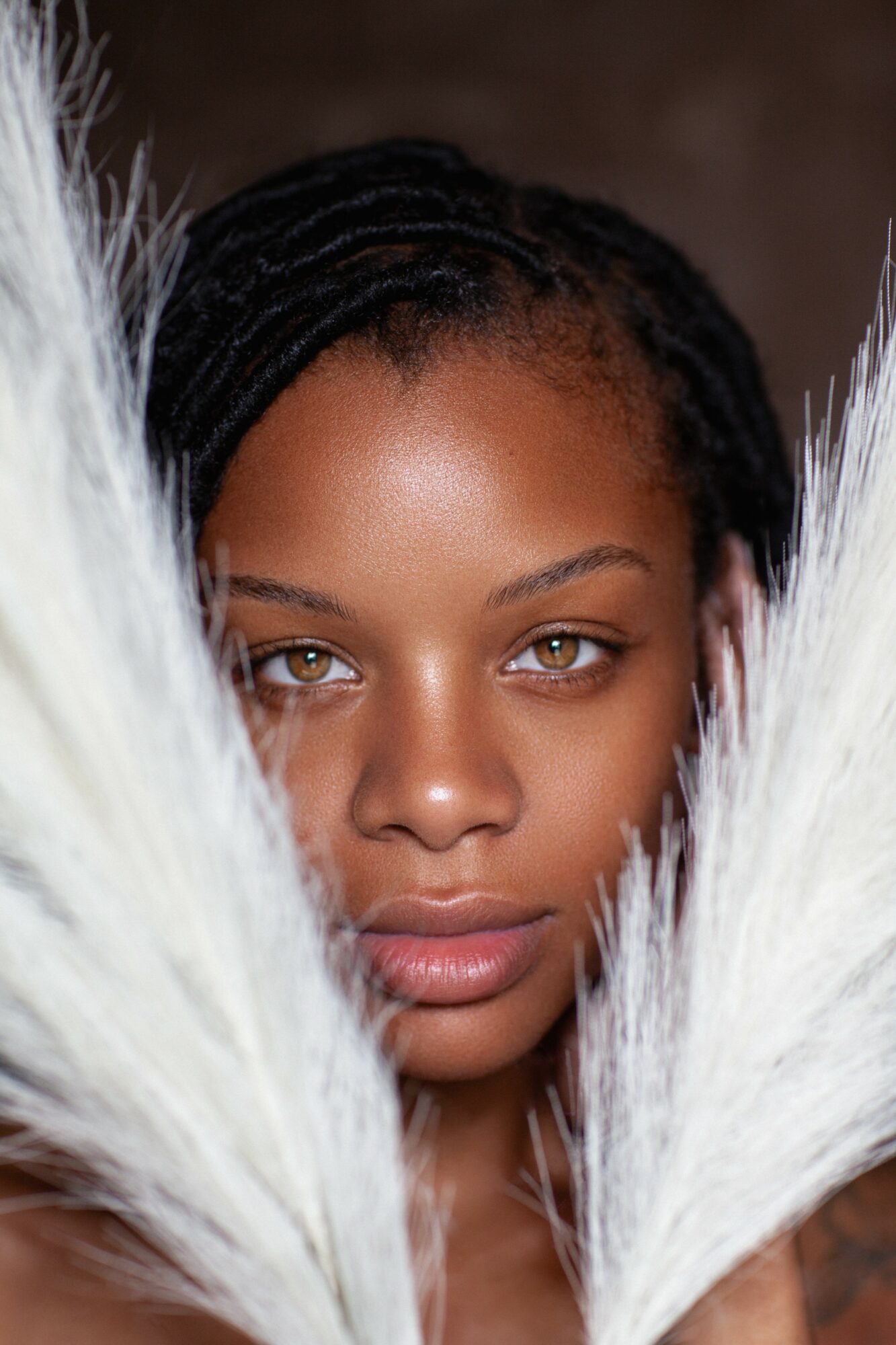 Close-up of a woman with braided hair surrounded by white feathers, looking directly at the camera.