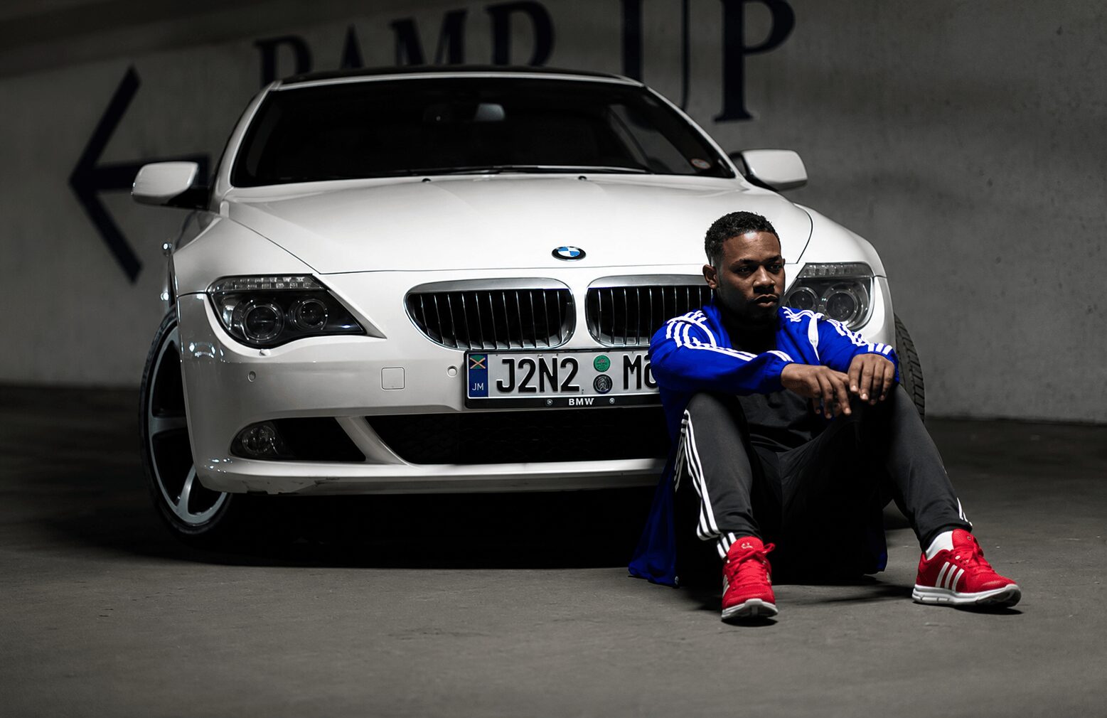 Man sitting on the ground in front of a white BMW car in a parking garage.