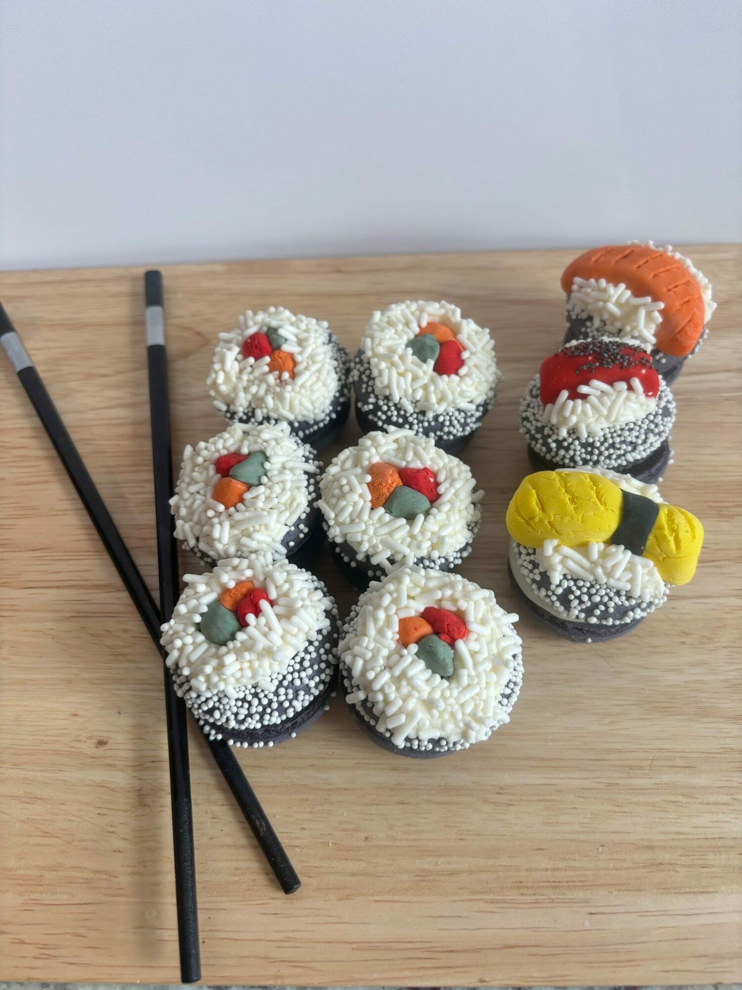 Sushi-shaped plush toys with rice, fish, and seaweed details, arranged on a wooden surface with chopsticks nearby.