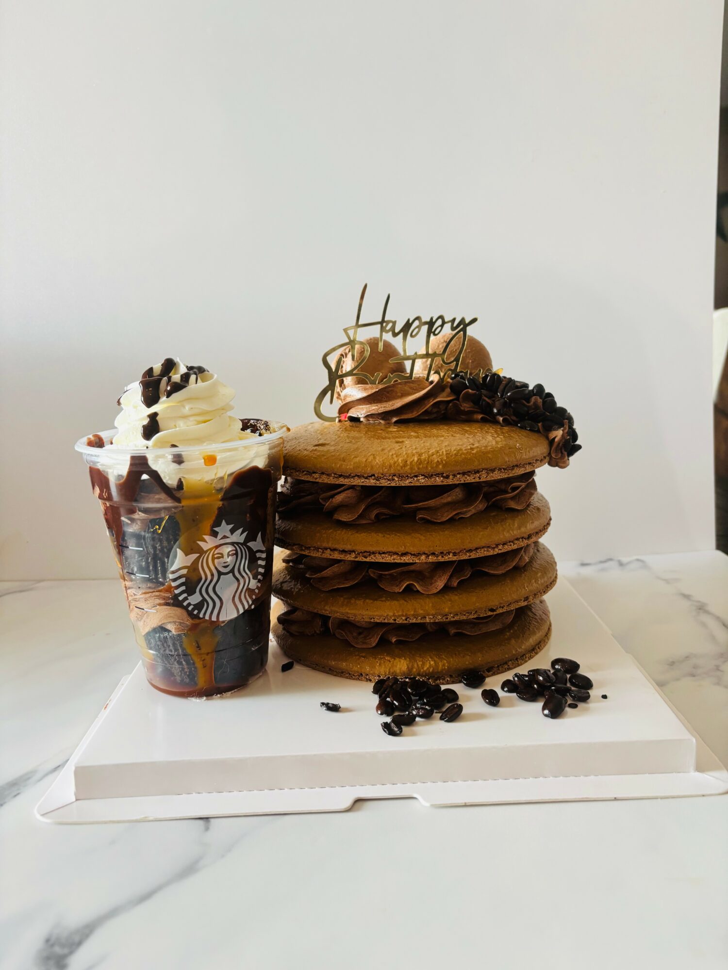 Stack of four caramel-colored cookies with chocolate chips, a small cup of whipped cream with sprinkles, and a 'Happy' topper, on a white surface.