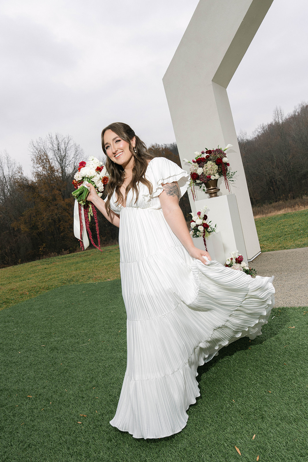 Young woman in a white dress holding a bouquet, standing outdoors near a modern white structure, smiling.