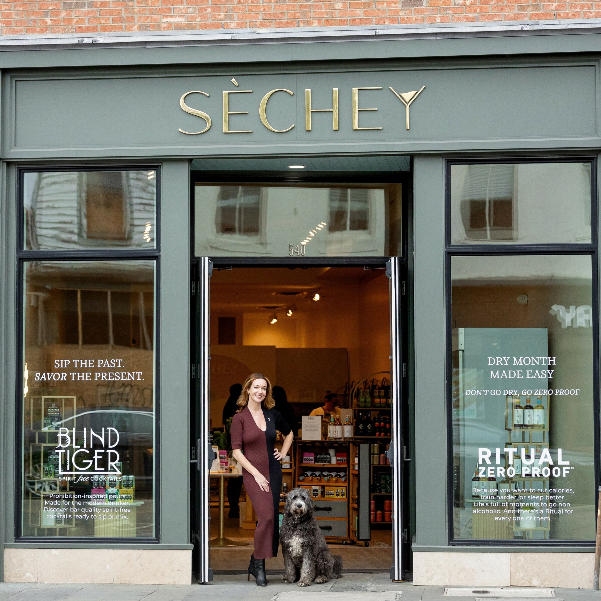 Woman standing in doorway of store named SÉCHEY, with shelves and products inside, and large windows on either side.