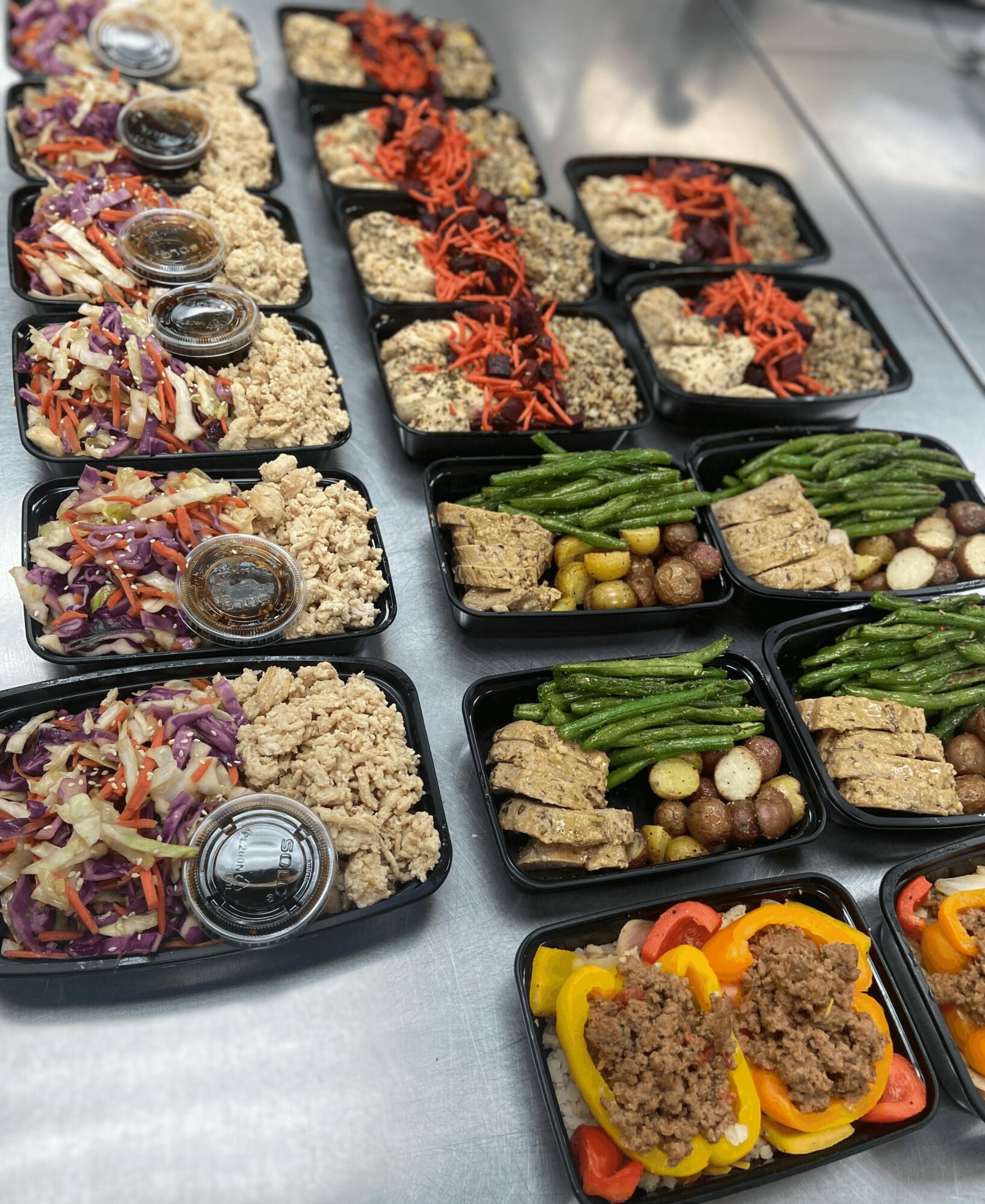 Assorted meal trays with rice, vegetables, and toppings arranged on a table, some with small containers of sauce or dressing.