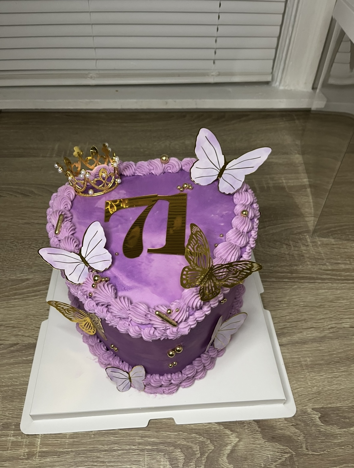 Heart-shaped purple birthday cake decorated with butterflies, a crown, and the number 7, on a white tray.