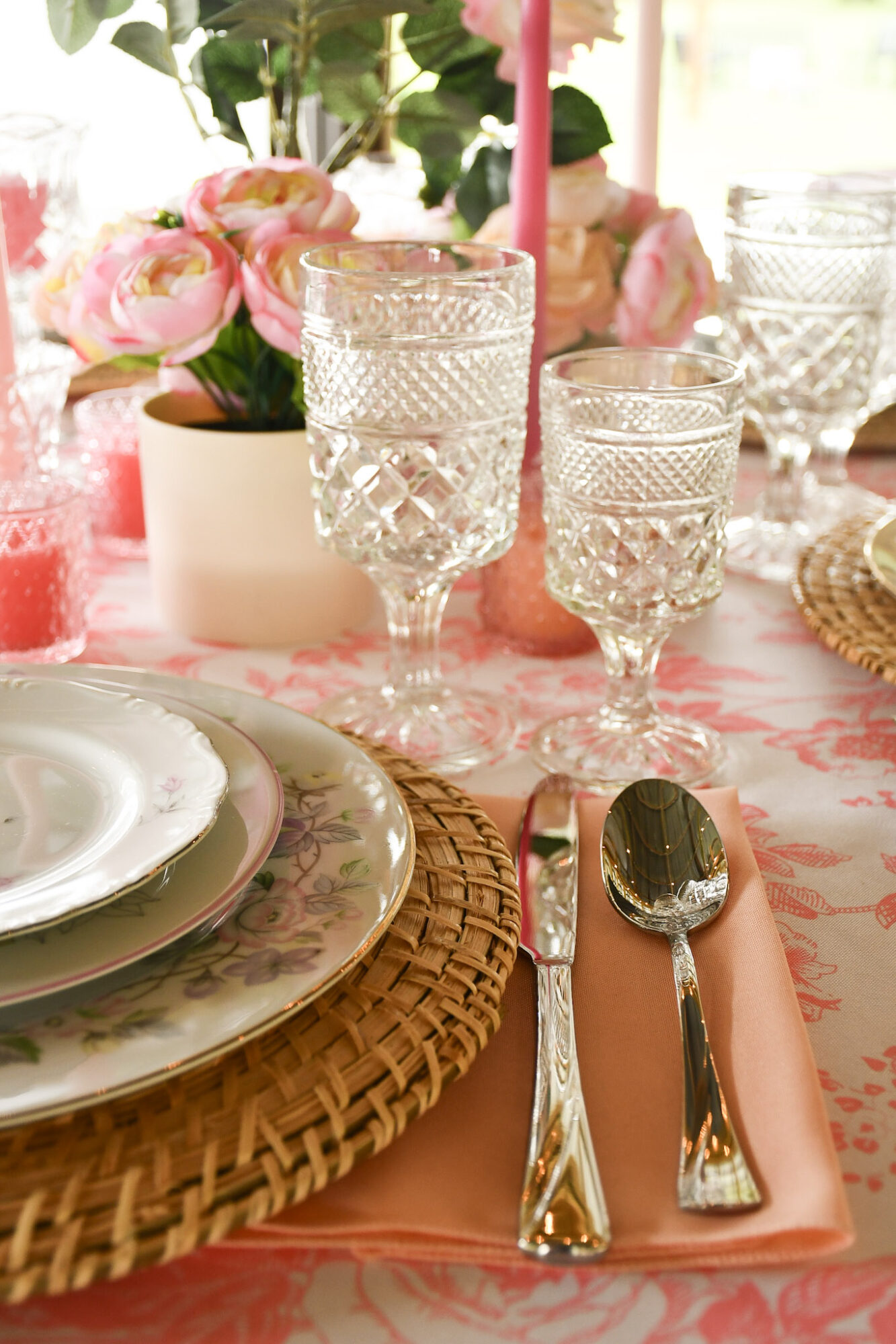 Table setting with floral centerpiece, glassware, plates, and cutlery on a pink tablecloth.