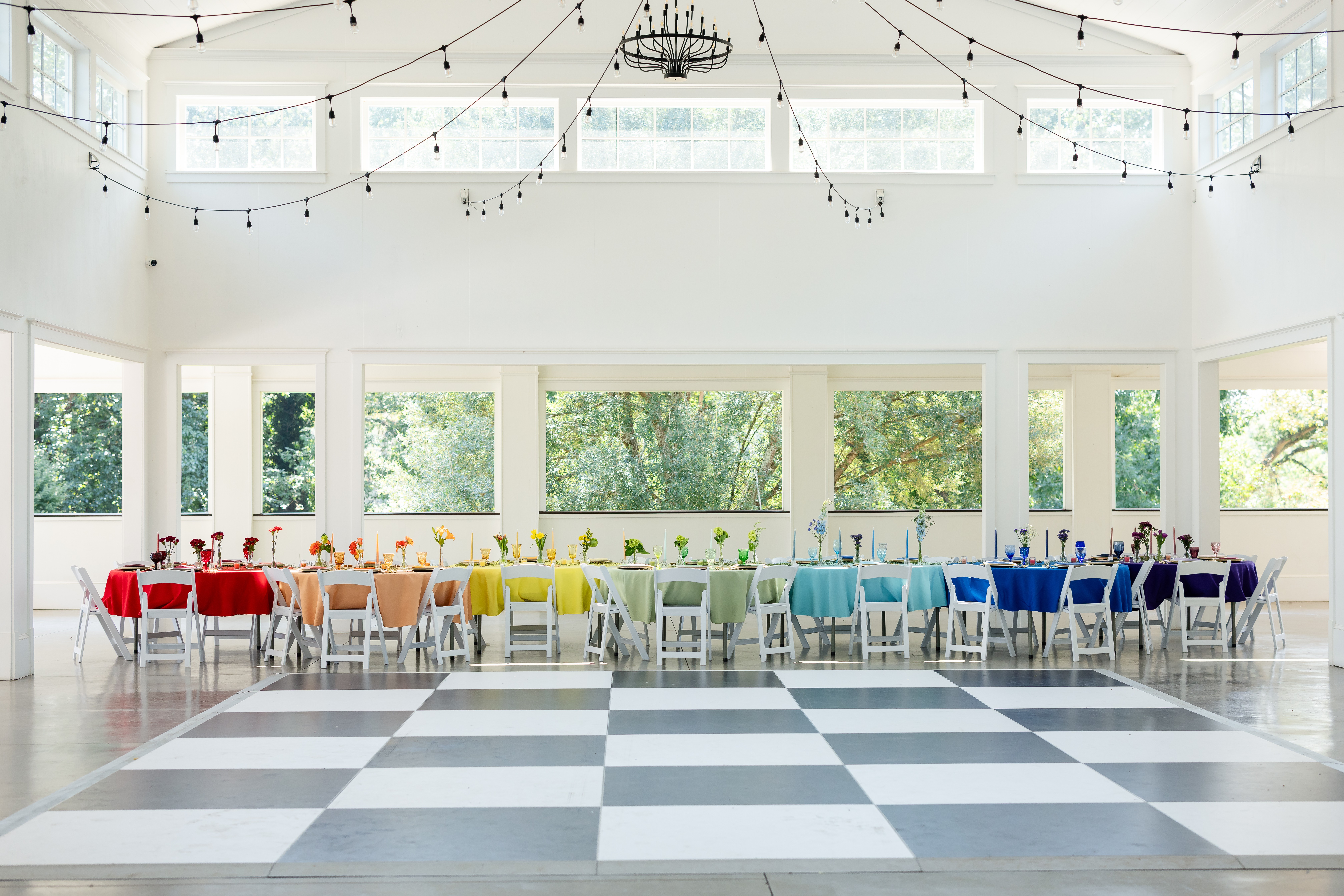 Long table with colorful chairs in a bright, spacious room with large windows and checkered floor.