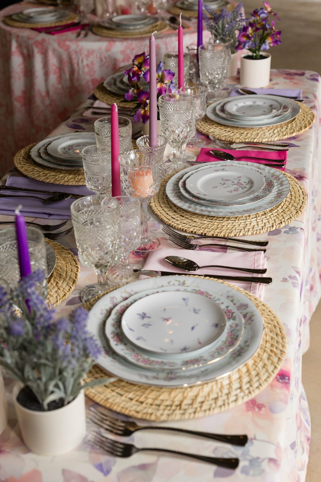 Table set with plates, glasses, pink candles, flowers, and woven placemats, decorated for a celebration or gathering.