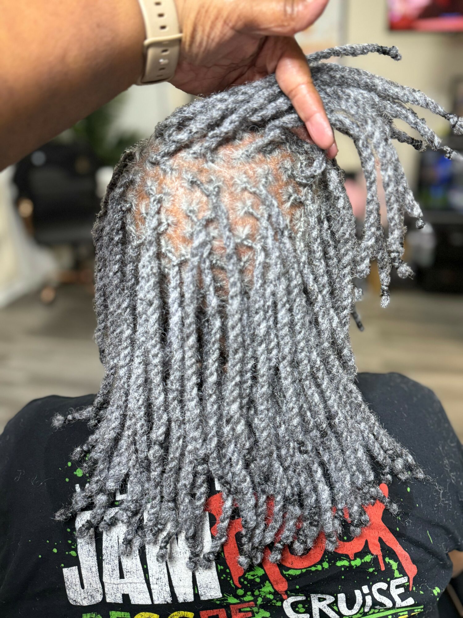 Person with gray dreadlocks viewed from behind, holding their hair up, in an indoor setting.