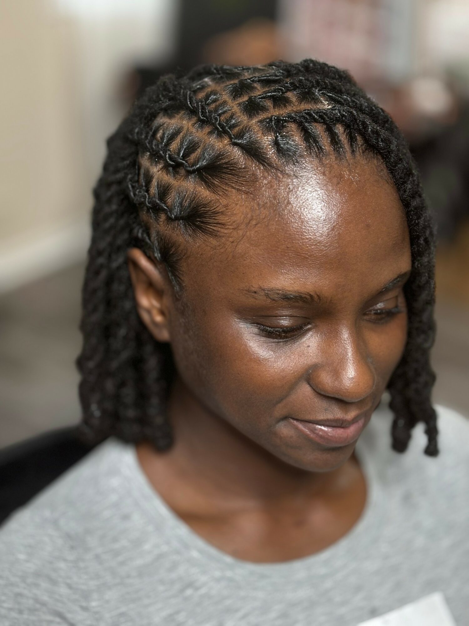 Close-up of a woman with braided hairstyle, looking downward, wearing a gray top.