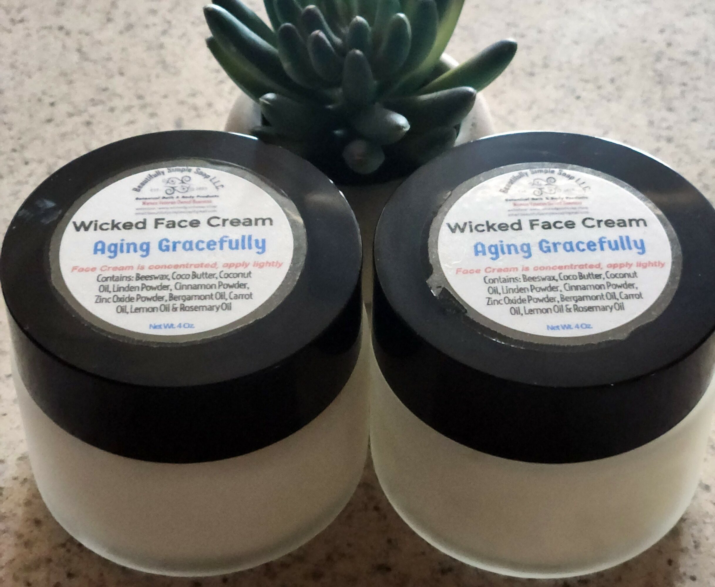 Two jars of Wicked Face Cream Aging Gracefully with a succulent plant behind them on a countertop.