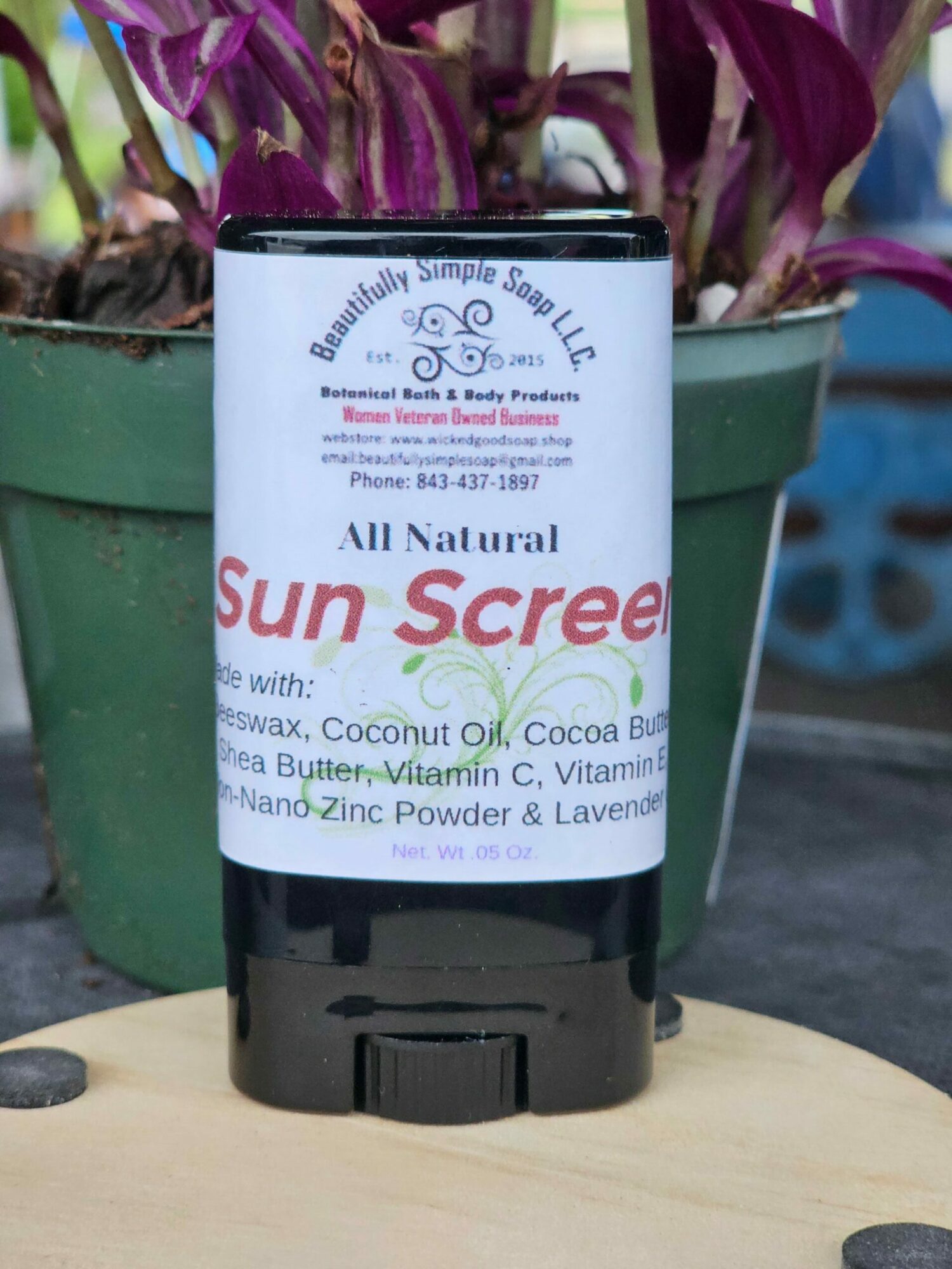 Black spray bottle with a white label, placed on a wooden surface, with a green plant in the background.