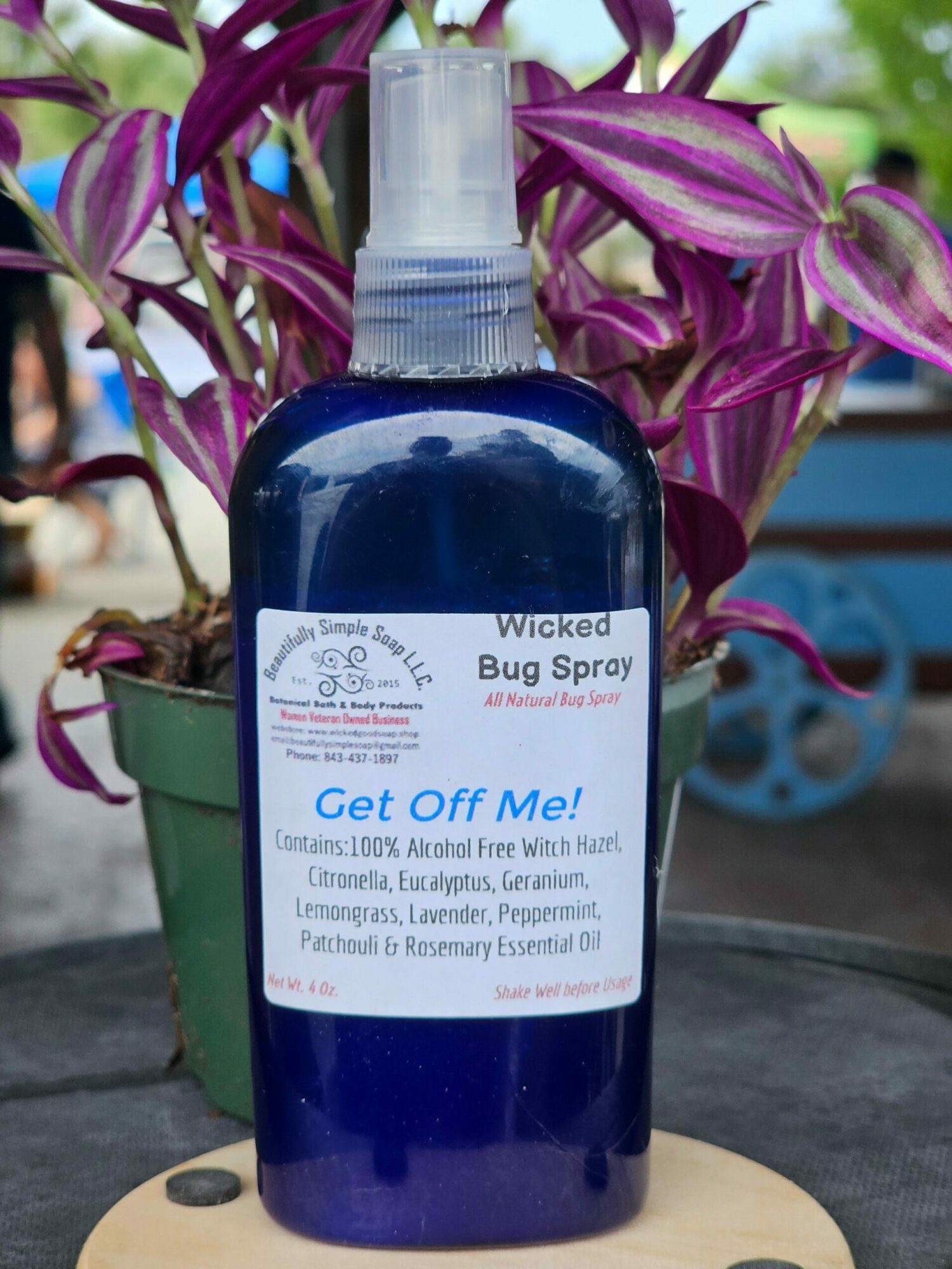 Blue spray bottle labeled 'Bug Spray' on a table with purple and green plants in the background.