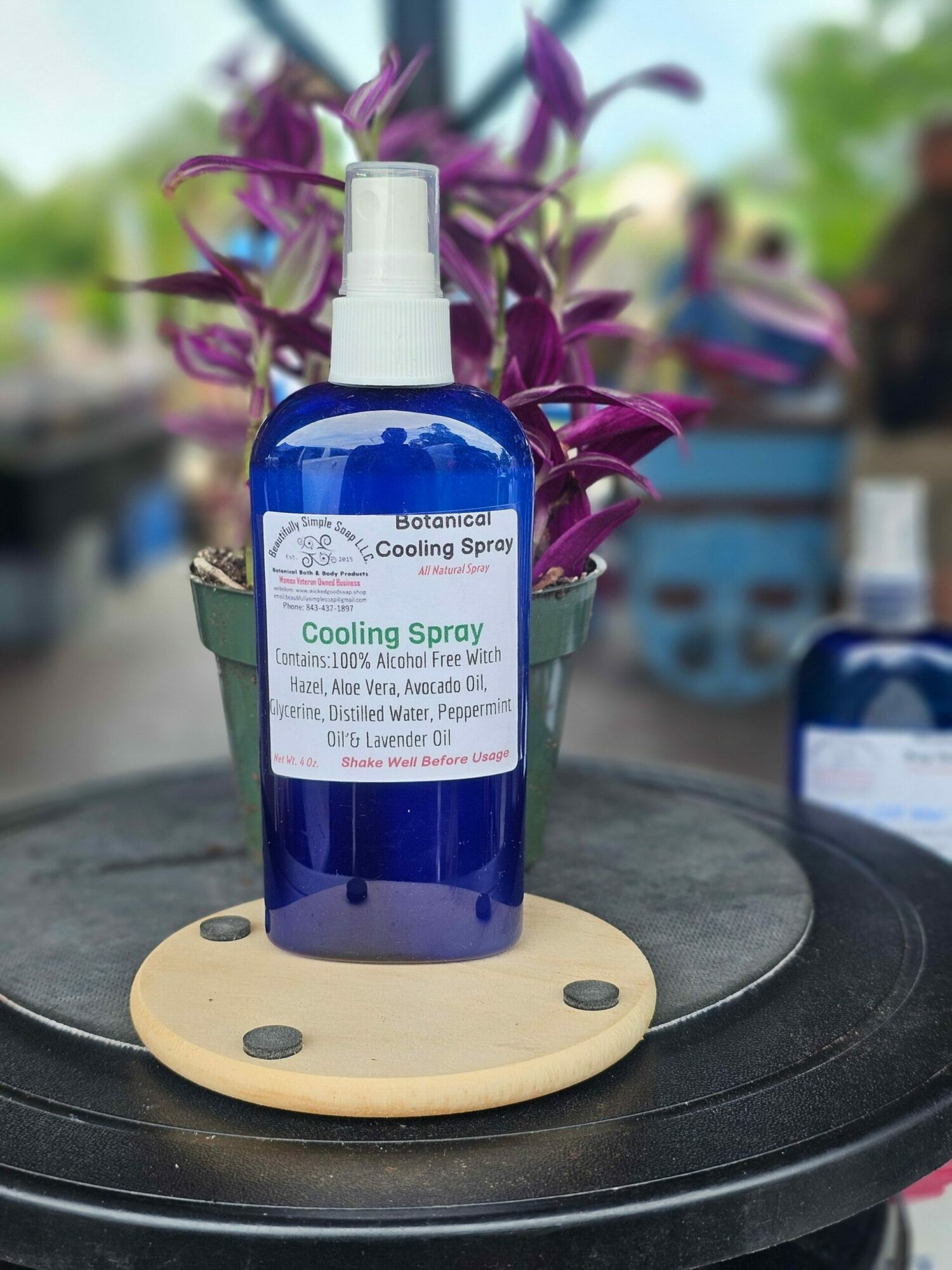 Blue spray bottle on a round black surface with purple flowers in the background.