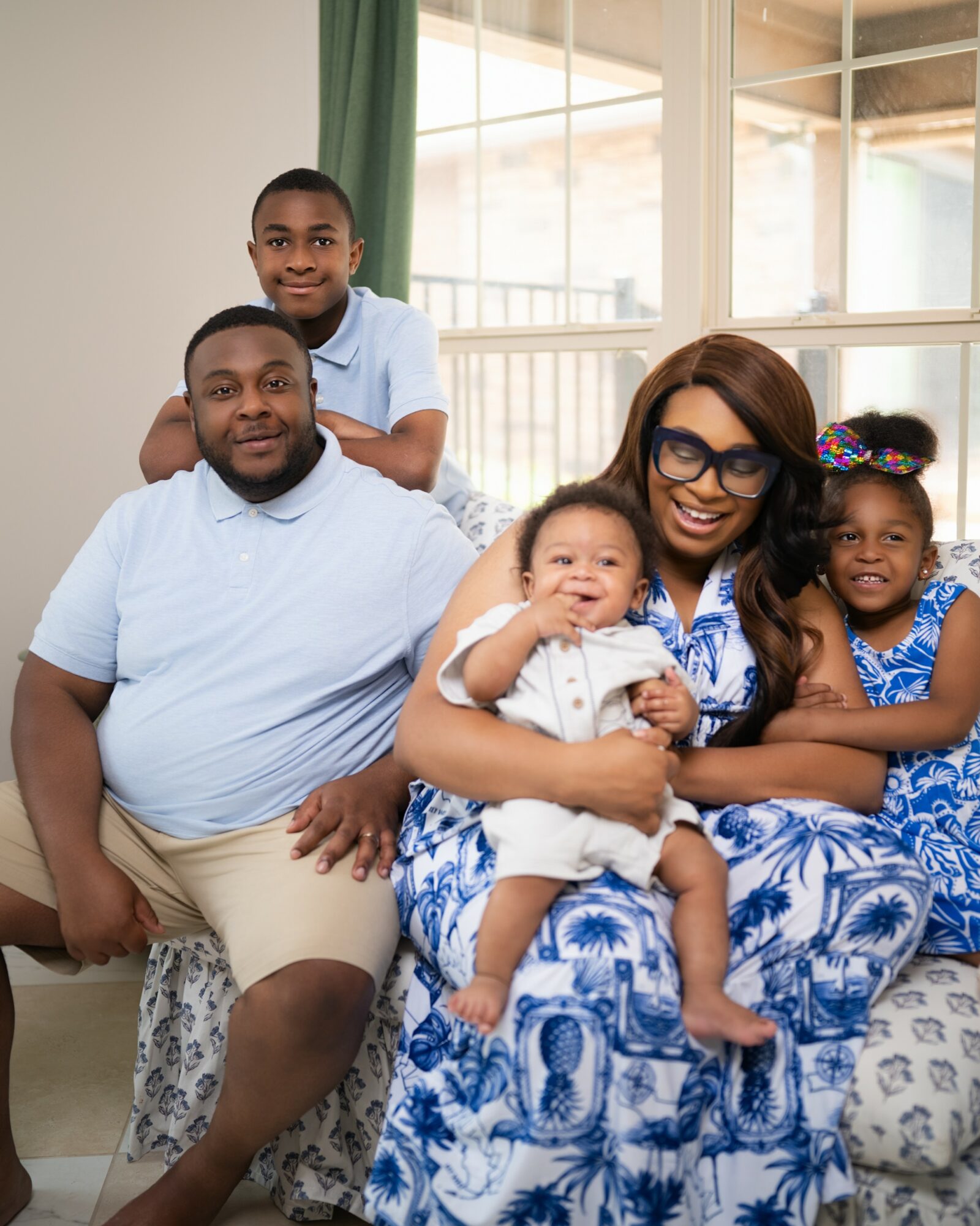 Family of five sitting on a sofa in a bright room with large windows, smiling and posing for the photo.