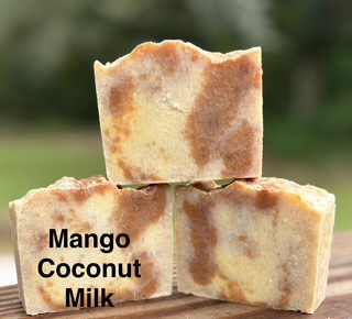 Three bars of soap with a marbled appearance, labeled Mango Coconut Milk, outdoors with blurred greenery background.