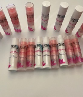 Multiple lip balm tubes arranged on a white surface, with some standing upright and others lying down, featuring pink and white packaging.