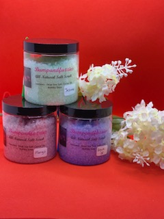 Three jars of colorful body scrub with white flowers on a red background.