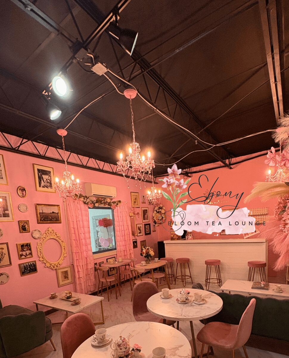 Interior of a pink-themed tea room with chandeliers, framed pictures, and round tables with chairs.