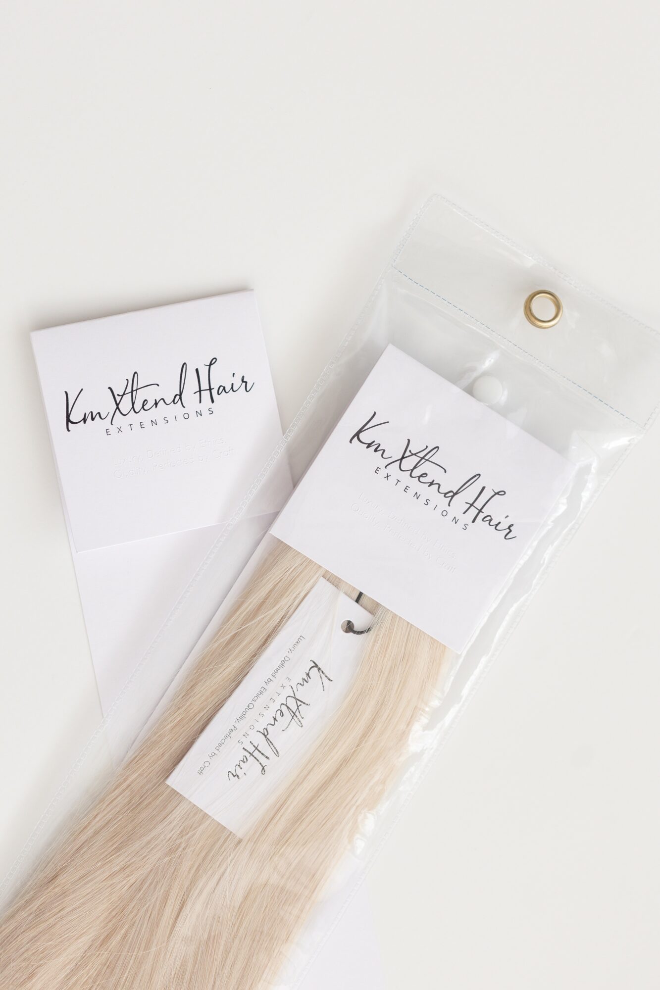 Blonde hair extension in clear packaging with white label, placed on white background.
