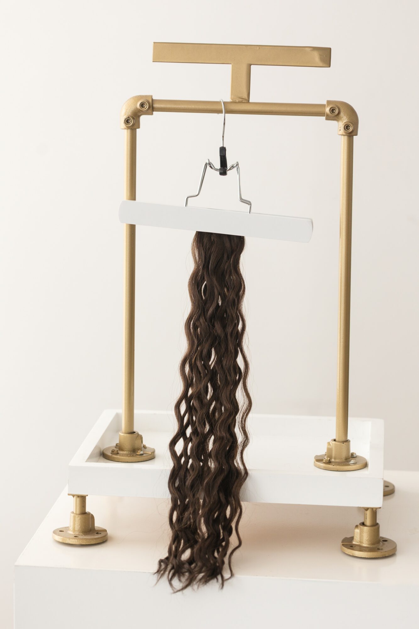 A hair extension hanging from a white and beige hair extension machine with a white base.