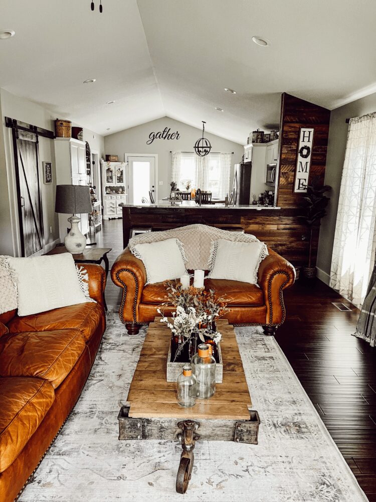 Living room with two leather sofas, a wooden coffee table, and a rug, leading to a kitchen area in the background.