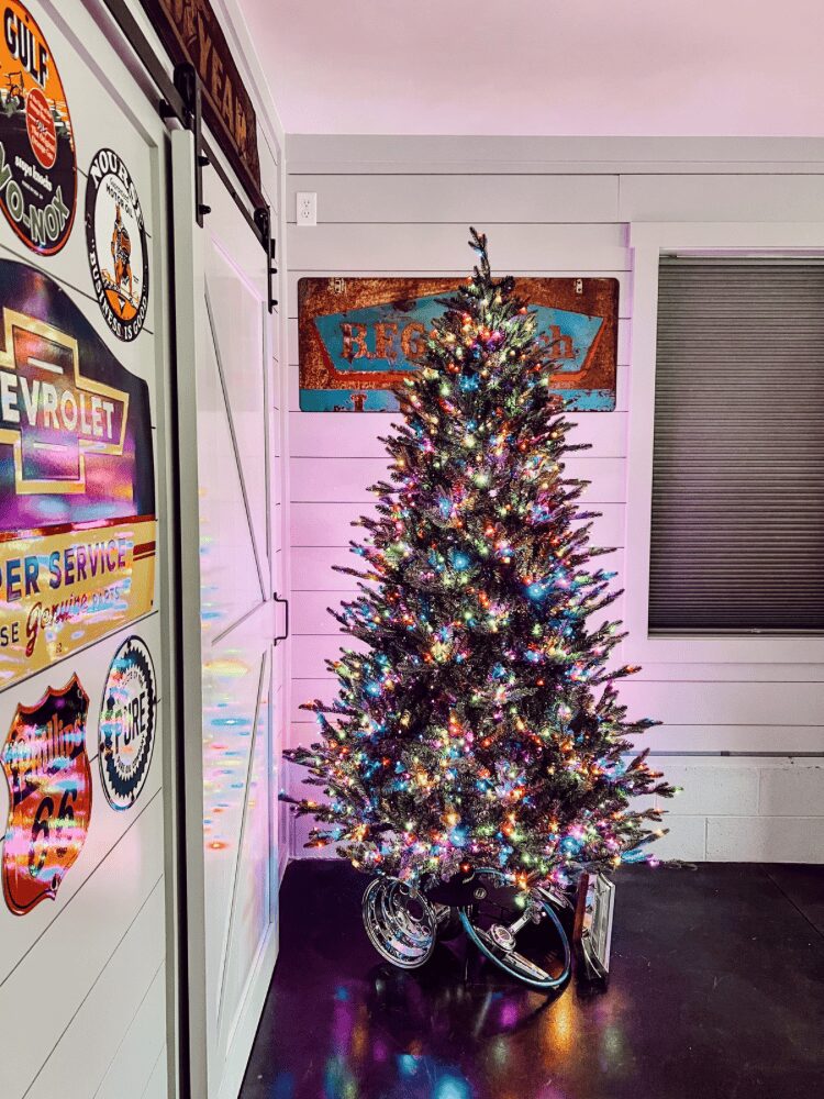 Decorated Christmas tree with colorful lights in a room with white walls and a window, bicycle at the base.
