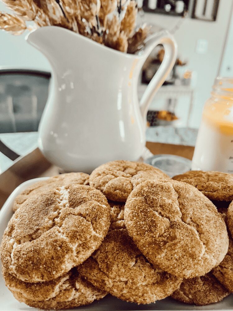 Close-up of cookies in front of a white pitcher and a glass of milk on a table.