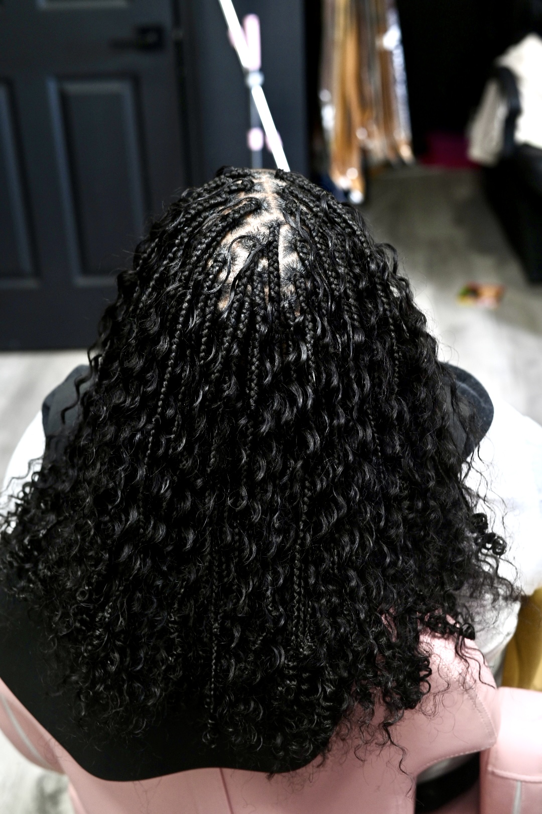 Back view of a person with curly, textured hair styled in twists, indoors with dark door and clothing in background.