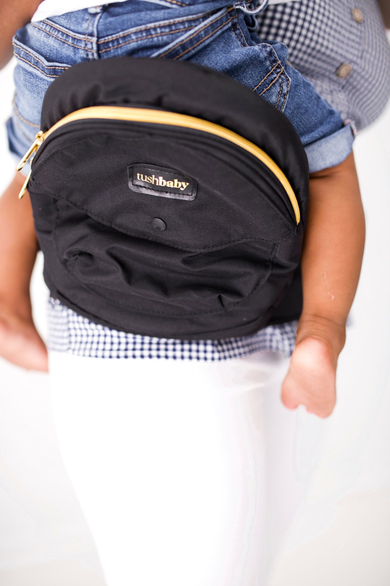 Child wearing a black backpack with yellow trim, denim jacket, and white pants, holding a small object in hand.