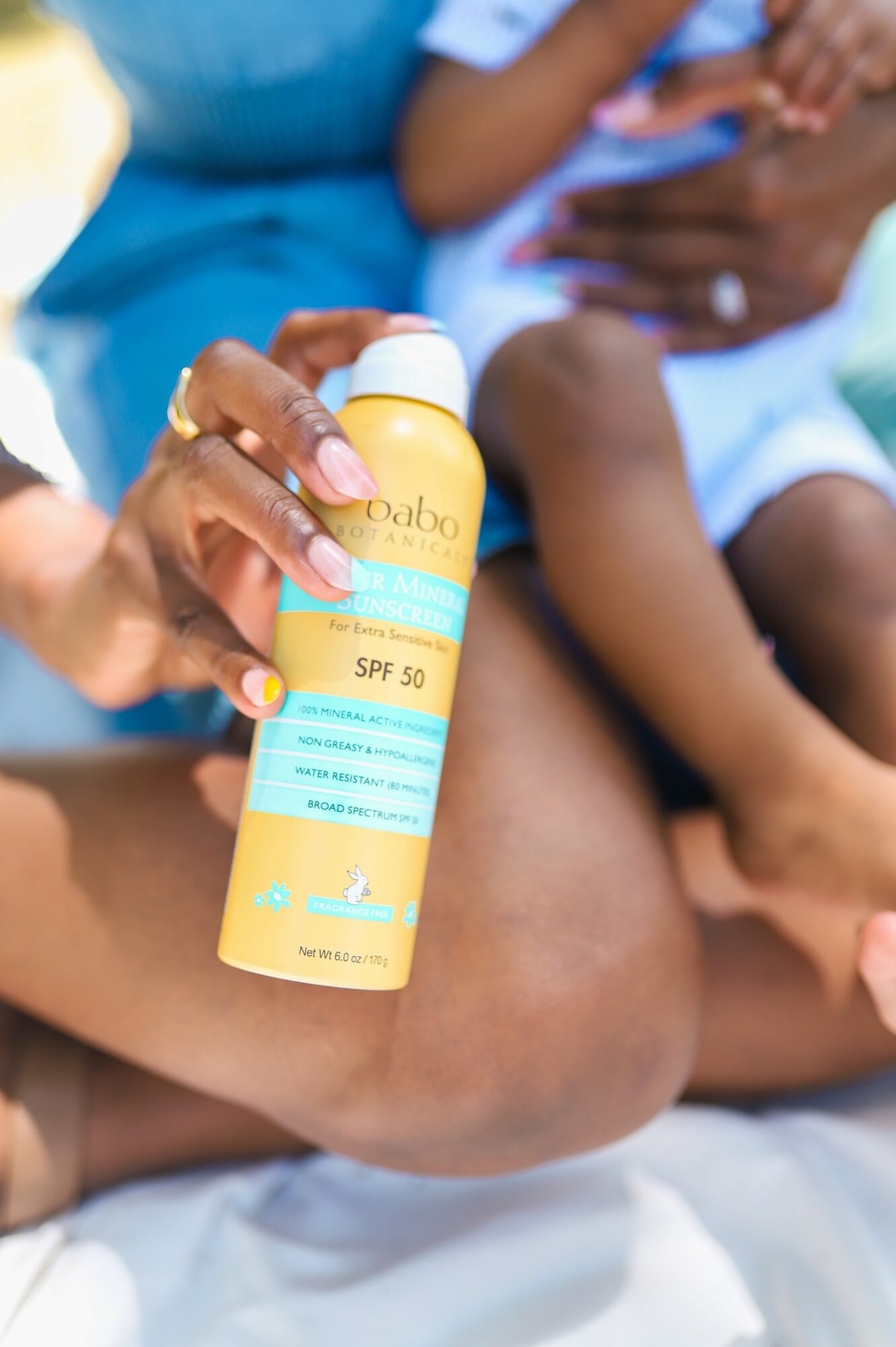Person holding sunscreen bottle with children in background, outdoors, sunny day.