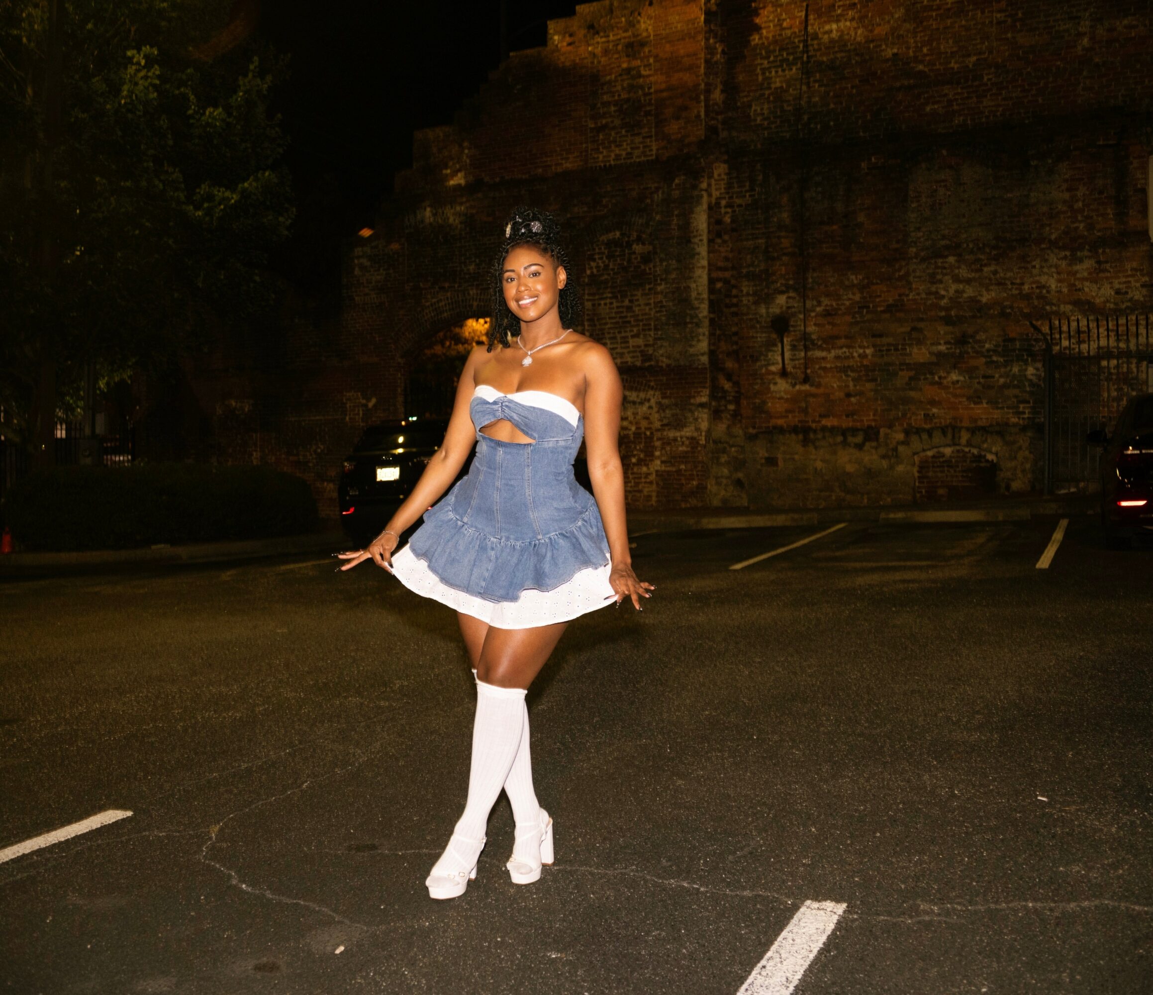 Young woman in a blue and white dress with white knee-high socks standing on a street at night.