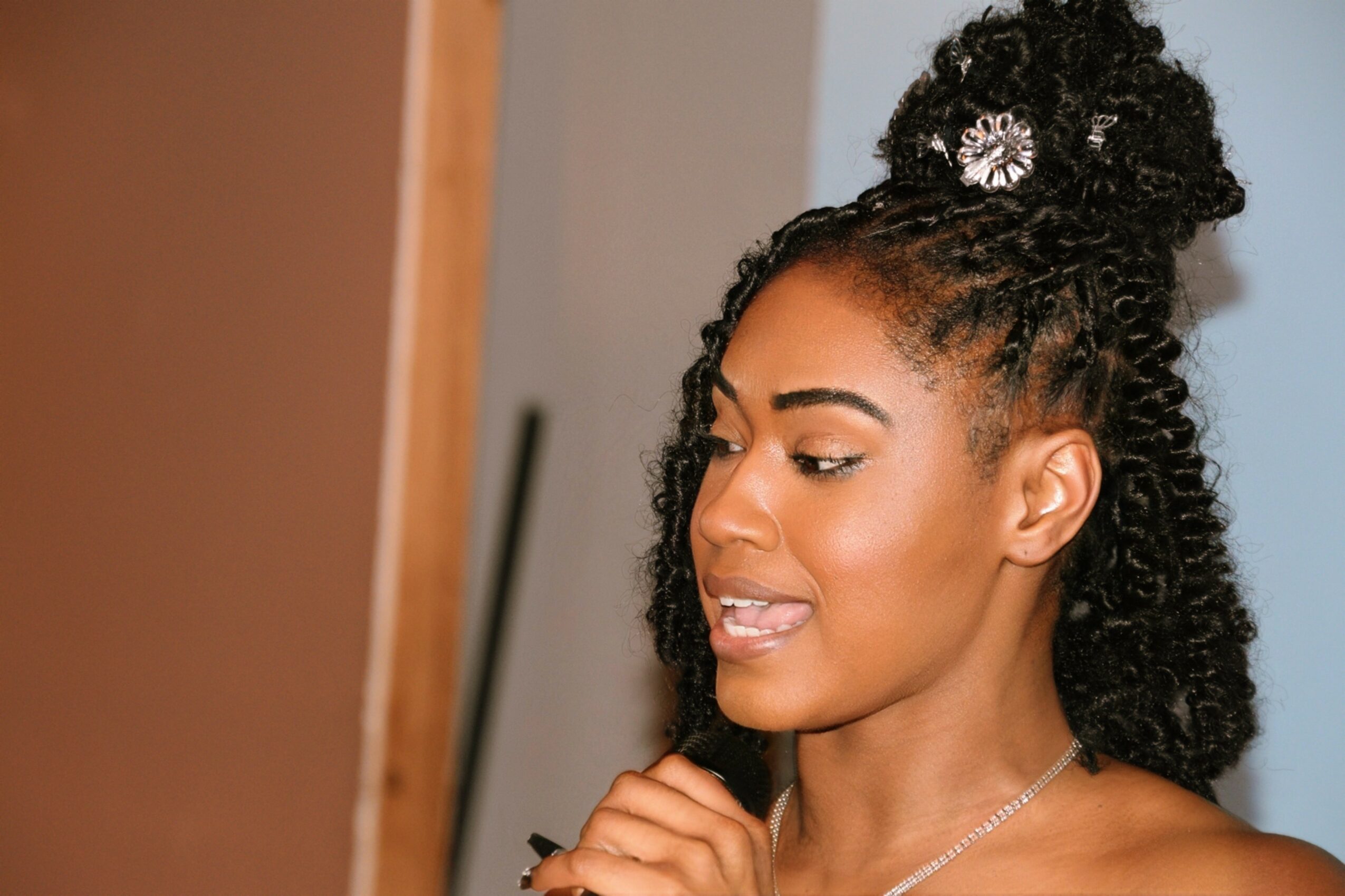 Young woman with curly hair styled in a high bun, smiling and looking to the side, wearing a necklace.