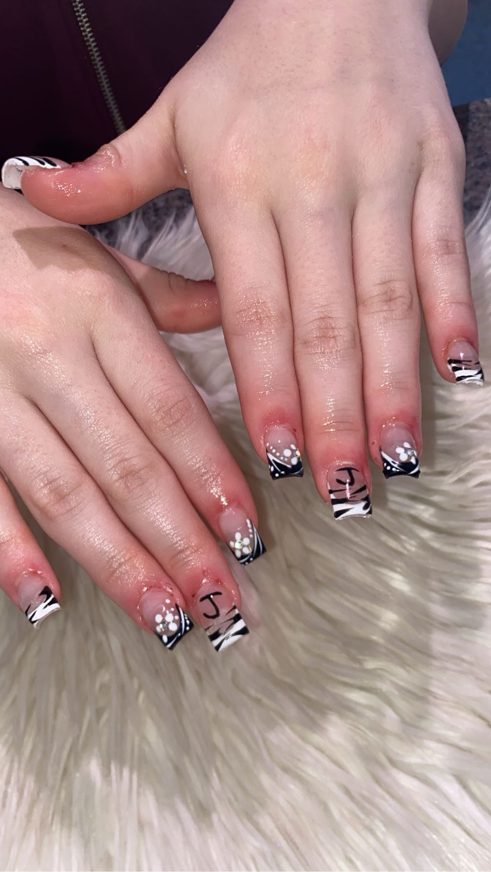 Two hands with decorated nails resting on a furry surface, nails have black, white, and silver designs with rhinestones.