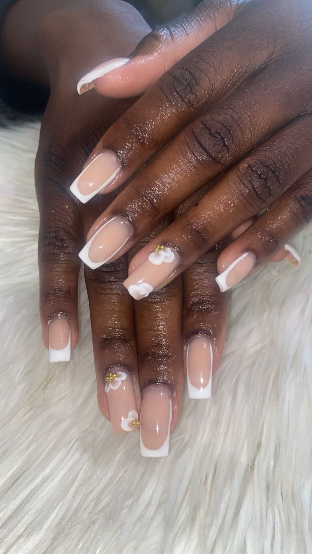 Two hands with manicured nails resting on a white furry surface, nails painted with light pink polish and floral designs.
