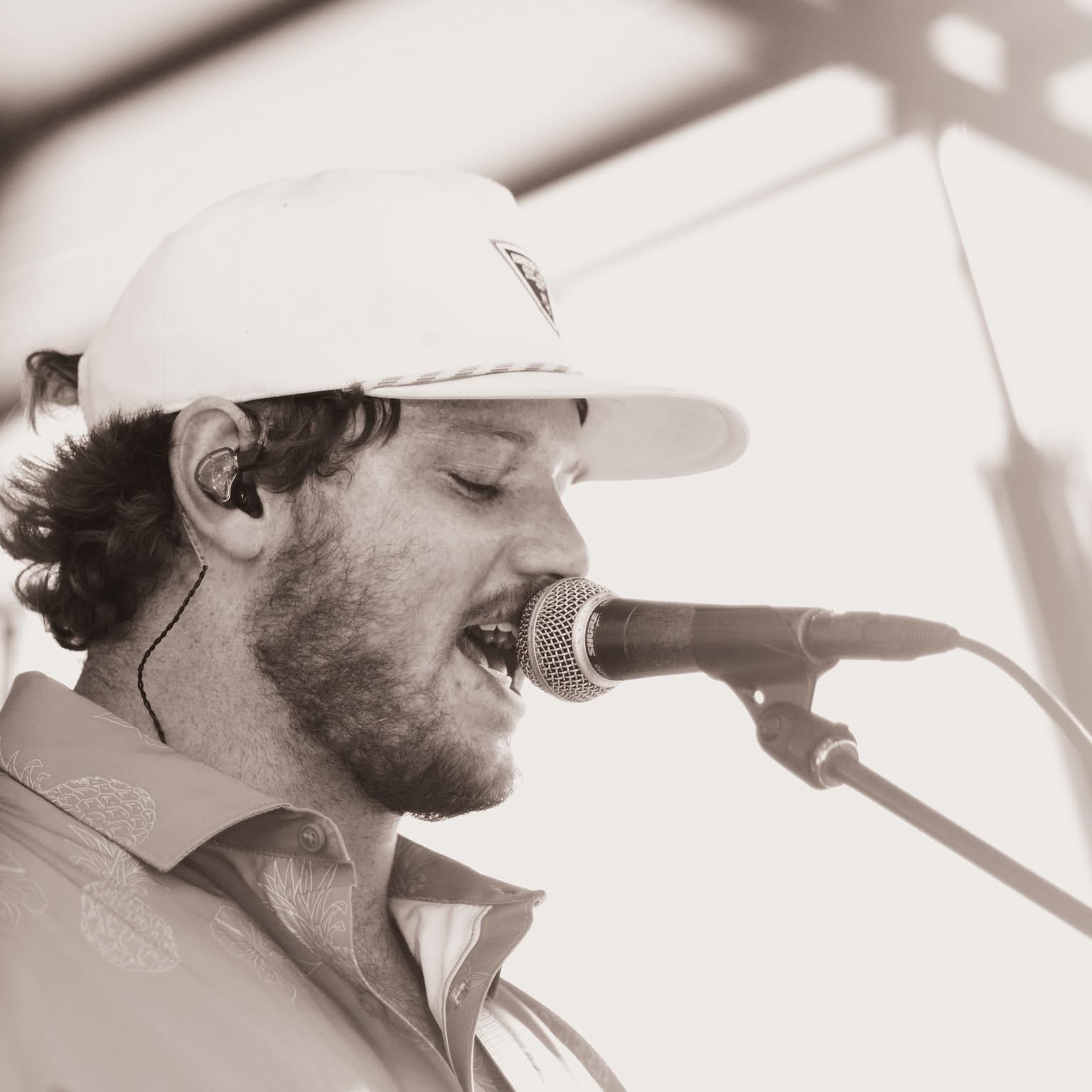 Man singing into a microphone, wearing a white cap and casual shirt, with a focused expression.