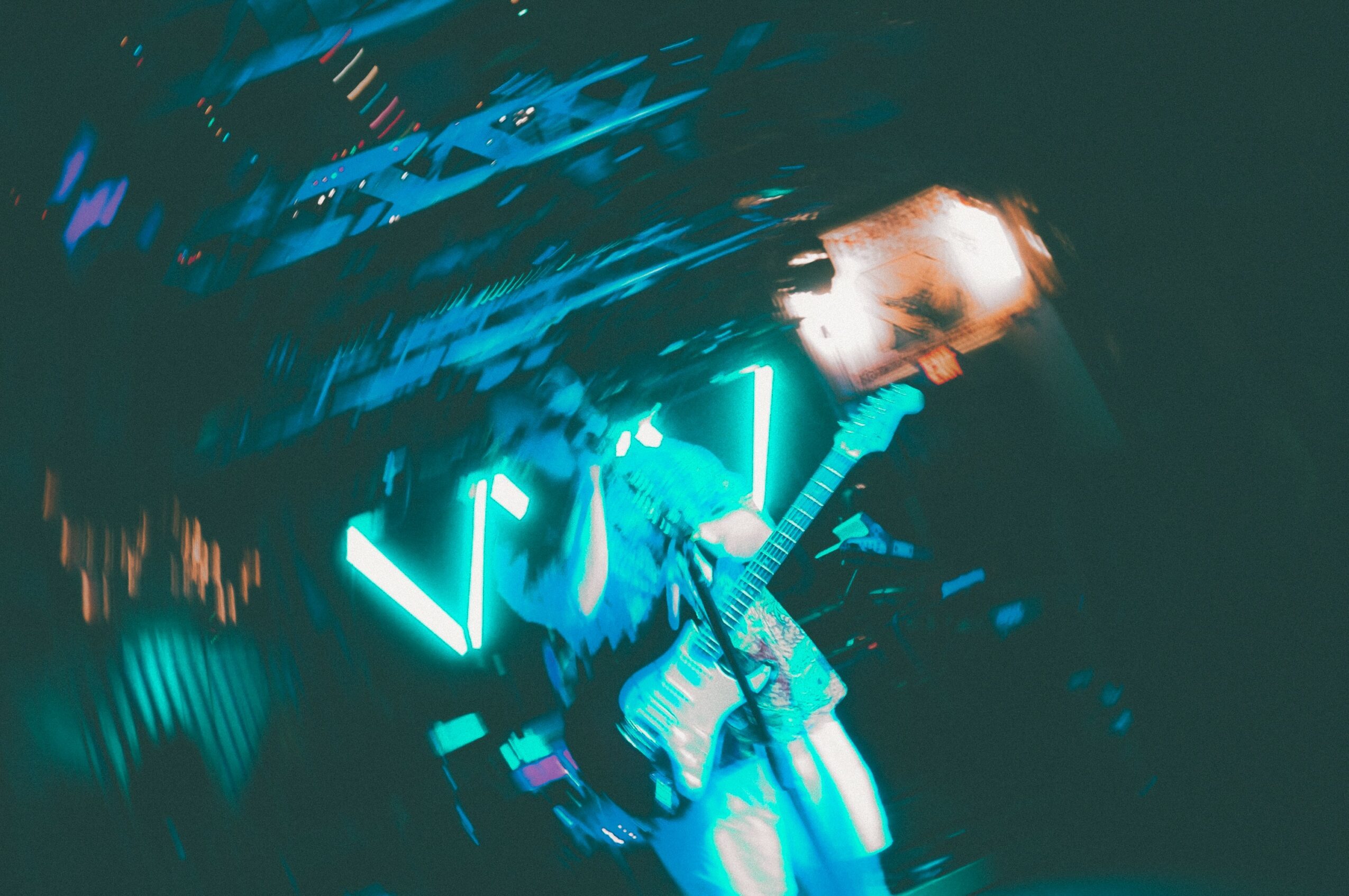 Person playing guitar on stage with bright neon lights, motion blur, and dark background.